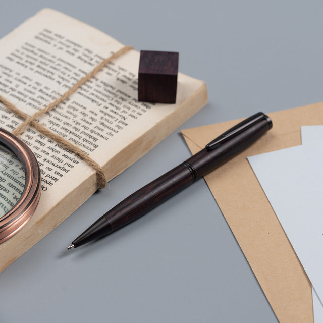 Gentlewood Studio tükenmez kalem koyu kingwood gövde, eski kitap ve büyüteçle masa üstü kurgusu