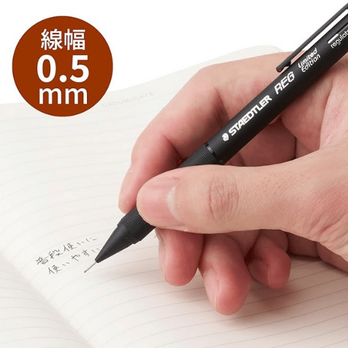 Staedtler REG kalemi elde tutuluyor, çizgili deftere yazı yazarken, çizgi kalınlığı 0.5 mm