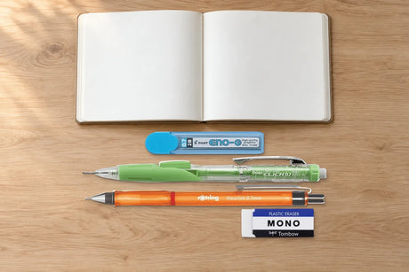 Açık ahşap masada boş defterin yanında Pilot Eno-G 0.7 mm 2B uç tüpü, Pentel Twist-Erase CLICK ve Rotring Visuclick versatil kalemler ile Tombow MONO silgi