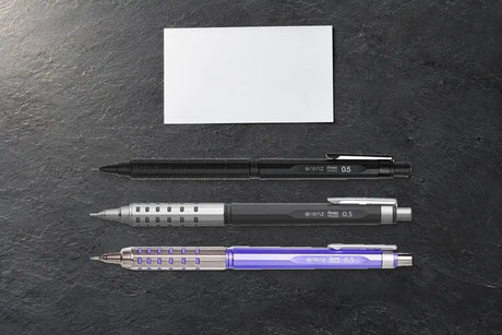 Koyu taş yüzeyde Pentel Orenz Nero, Orenz AT Gri ve mor Orenz AT Limited versatil kalemler