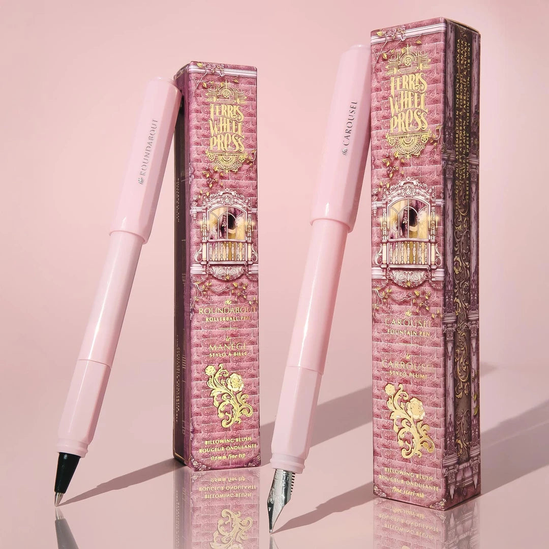 Billowing Blush serisinin pembe Roundabout rollerball ve Carousel dolma kalemi, desenli kutularıyla pembe zeminde