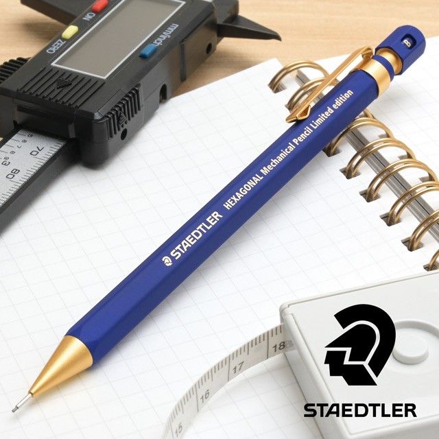 Staedtler Hexagonal kalem masa üstü kurgusu, kareli defter, dijital kumpas ve şerit metre yanında
