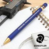 Staedtler Hexagonal kalem masa üstü kurgusu, kareli defter, dijital kumpas ve şerit metre yanında