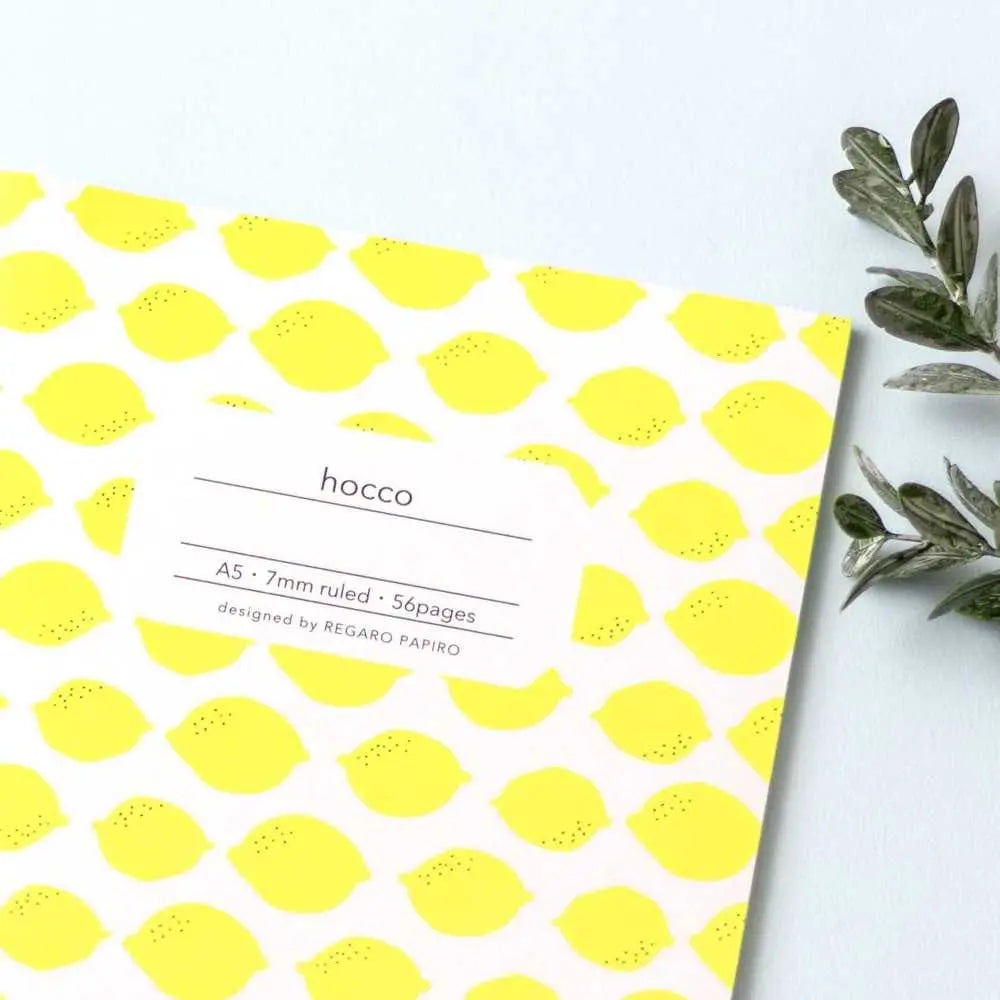 Apica Hocco limon desenli defter açık mavi zeminde, yanında yeşil zeytin dalı, çapraz çekim