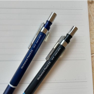 Kitera KS-01 lacivert ve siyah iki kalemin üst gövdeleri, çizgili defter üzerinde yan yana