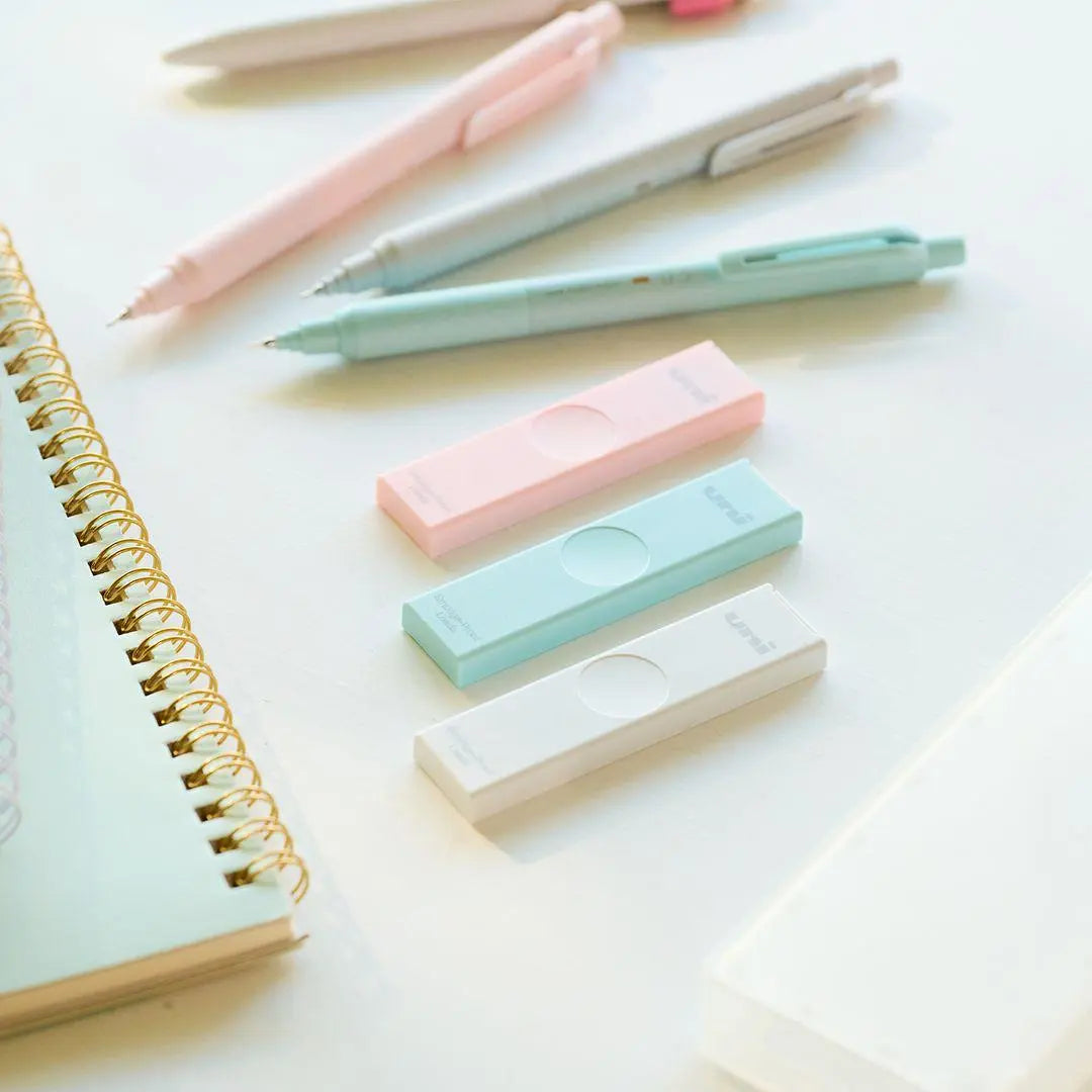 Uni HB kalem ucu kutuları masa üstünde, yanında pastel renkli kalemler ve spiralli defter