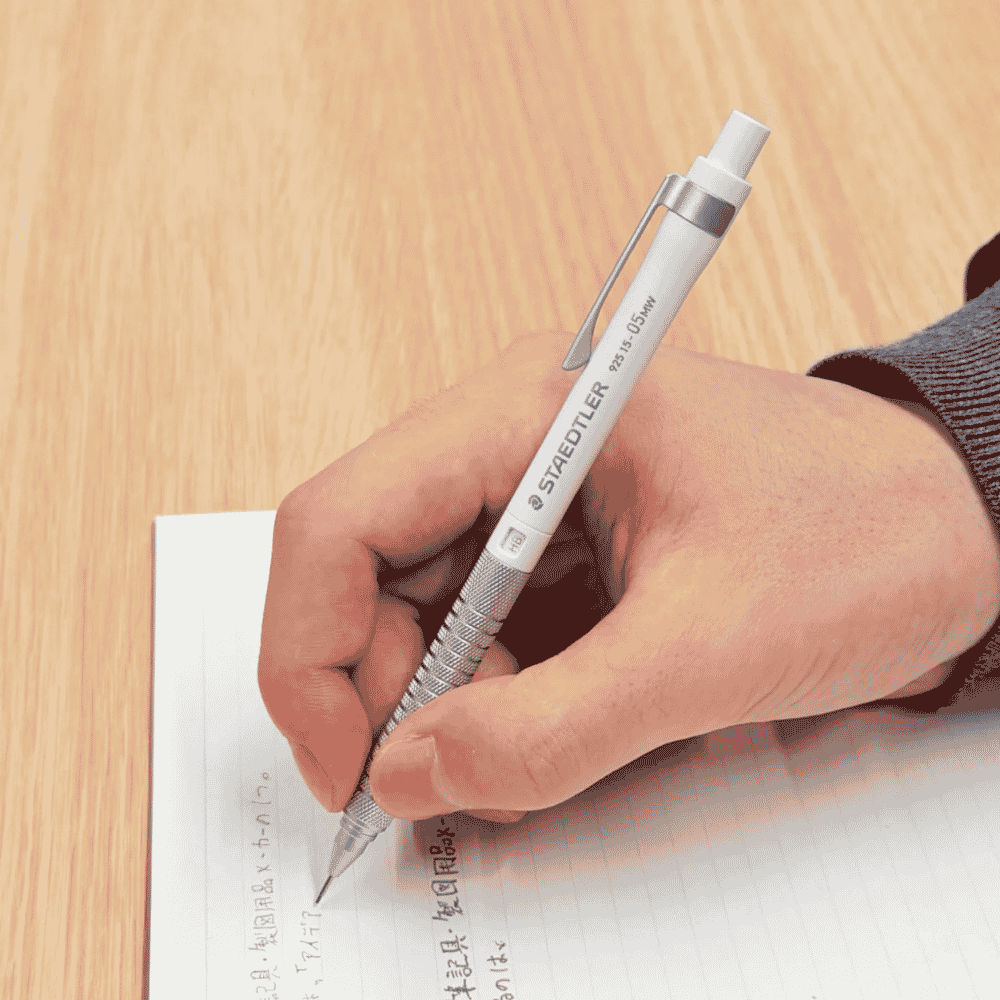 Staedtler 925 15 kalemi elde tutuluyor, ahşap masada çizgili kağıda Japonca not yazılıyor