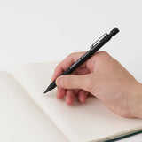 Staedtler Hexagonal kalemin siyah versiyonunu tutan el, çizgili açık defter üzerinde yazarken
