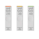 Uni Smudge-Proof 0.5 mm uç tüpleri yan yana; 2B, 3B ve 4B sertlikler turuncu, sarı ve yeşil kapaklı